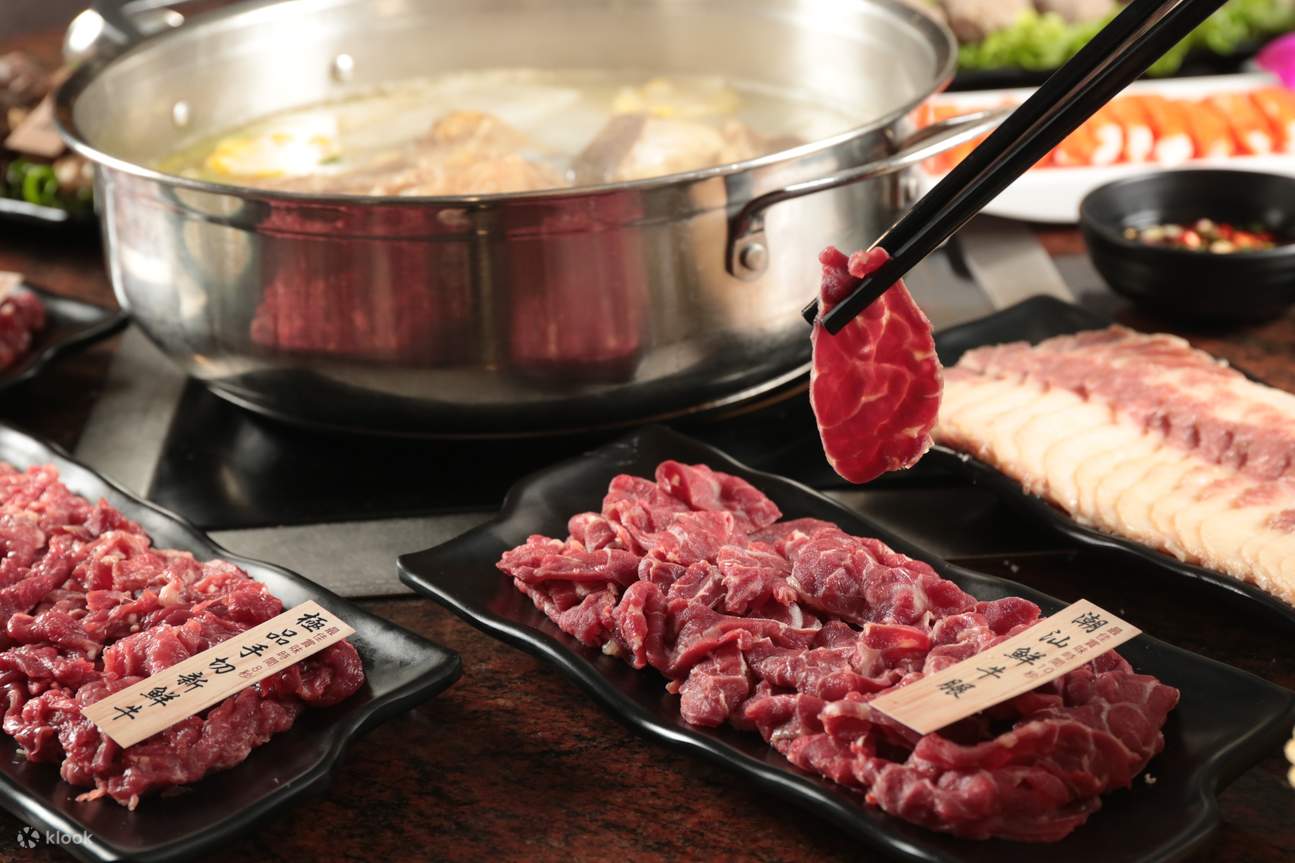 Plates of raw meat are arranged around a hot pot with seafood in a restaurant featuring retro decor, embodying Hong Kong's authentic and affordable dining culture in Mong Kok.